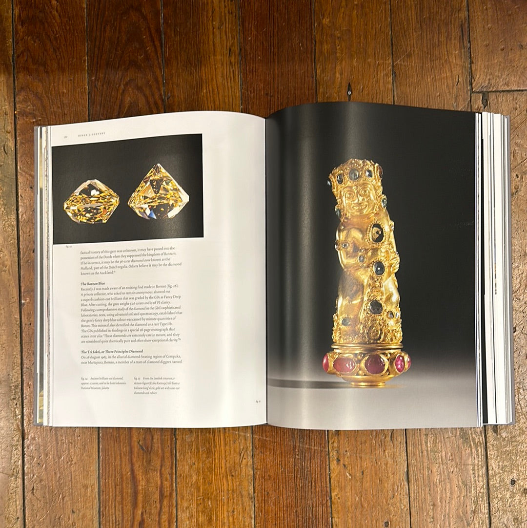 Open book on wooden surface showing detailed images and descriptions of ancient gold and gemstone artifacts, featured in Diamonds Across Time: Facets Of Mankind.