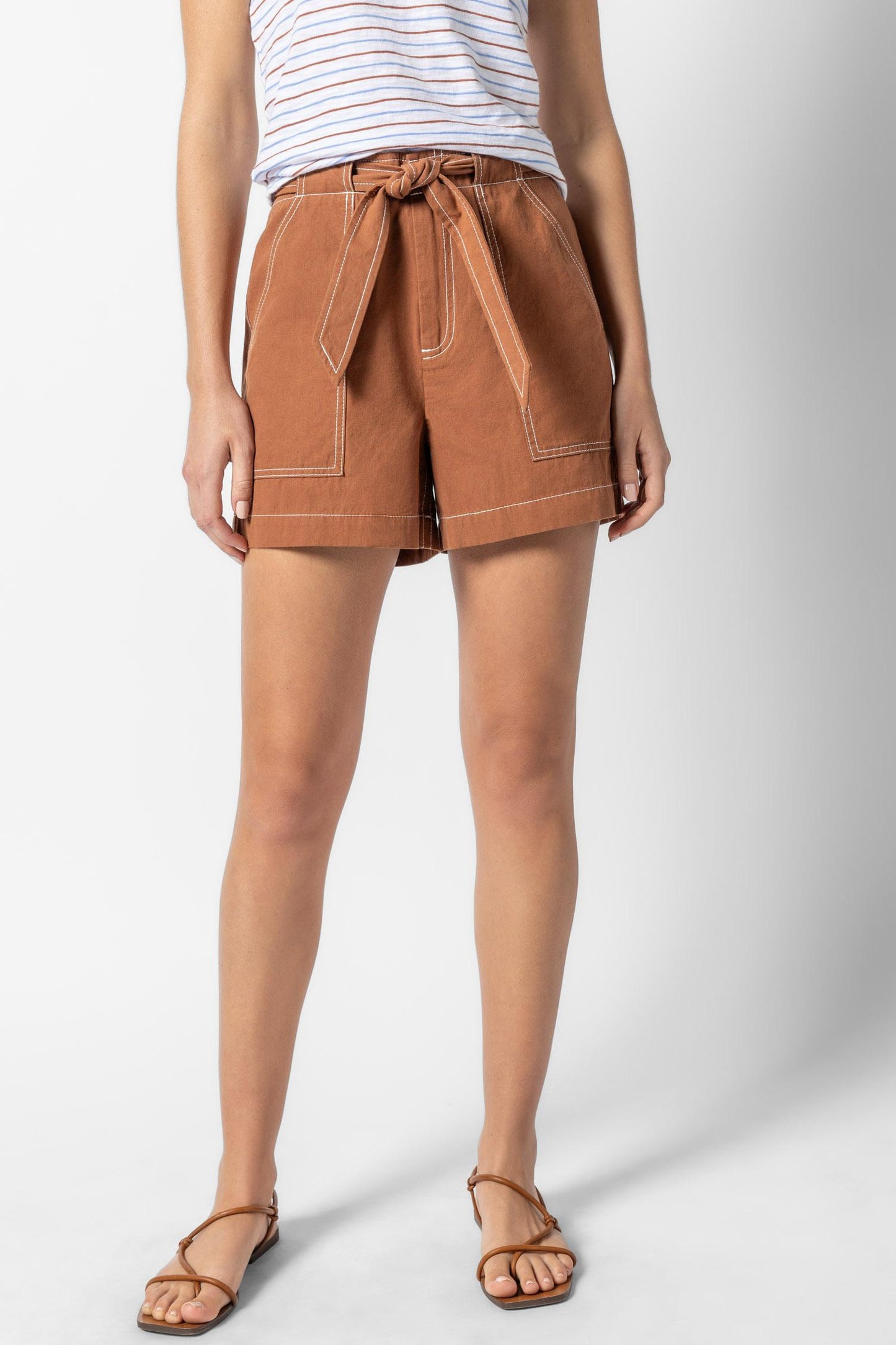 Woman wearing rust-colored Belted Canvas Short with front patch pockets and a tied waist belt, styled with a striped tank top and brown sandals.