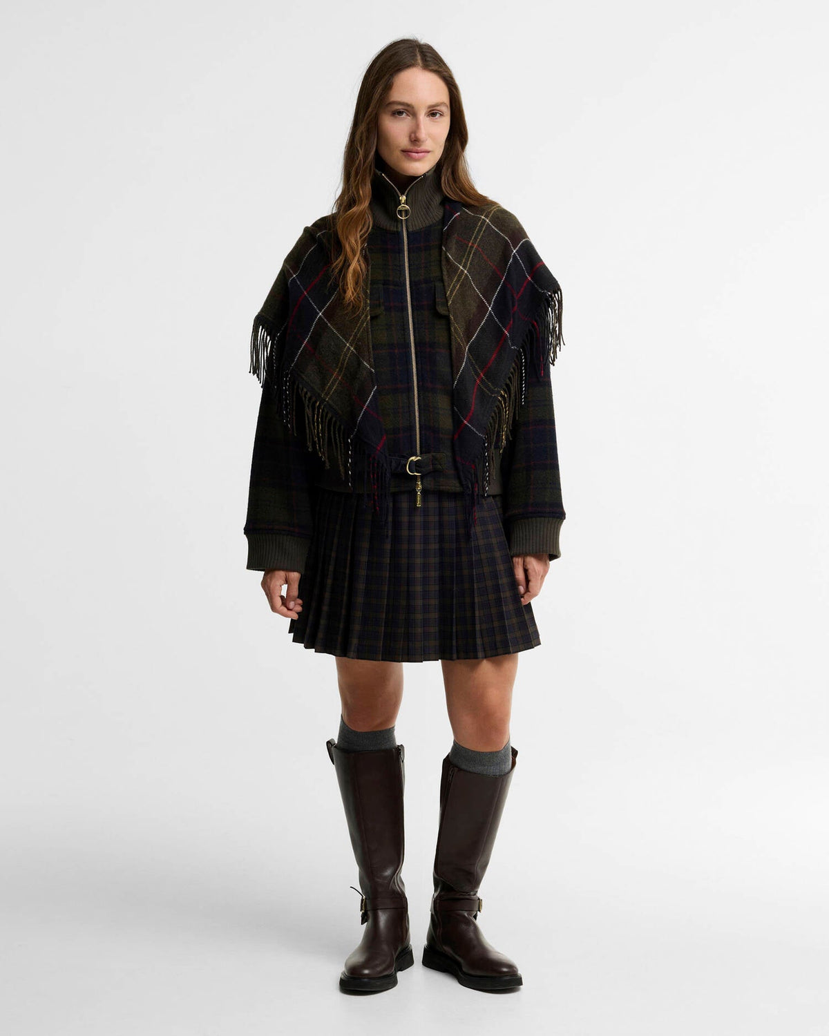Woman wearing a tartan poncho, pleated skirt, and tall dark boots