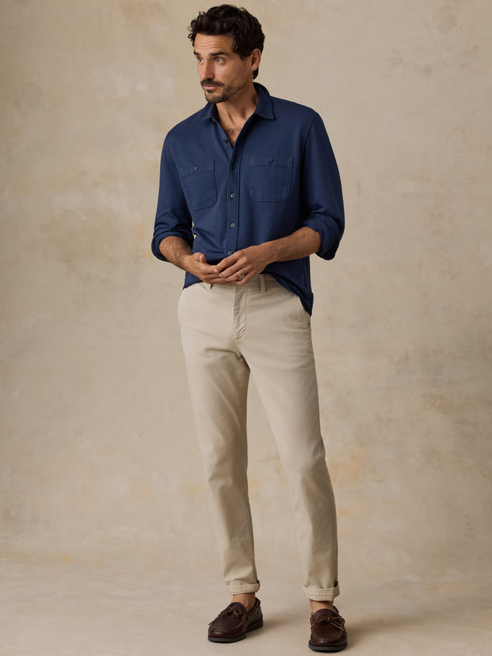 Man wearing a navy button-down shirt and beige pants against a neutral backdrop
