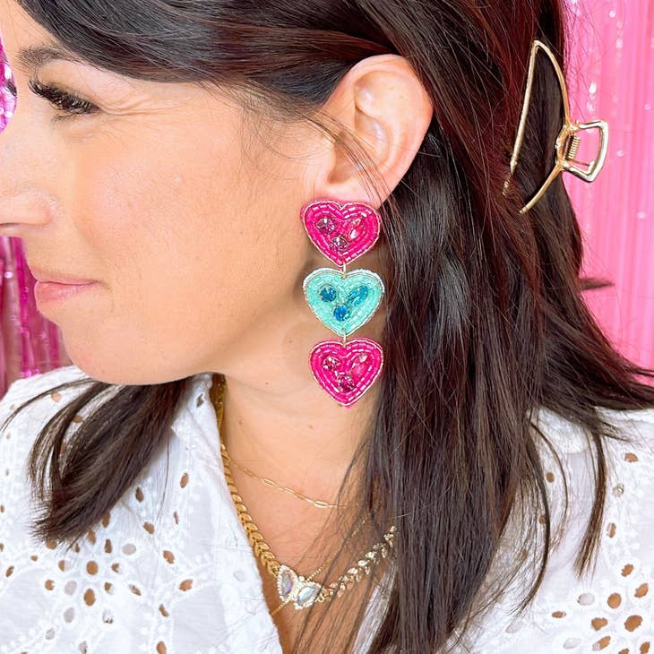 Close-up of a woman wearing vibrant Triple Sweet Heart earrings featuring two pink hearts and one blue heart, styled with a delicate butterfly necklace and gold hair clip, showcasing boutique jewelry with authentic Hill Country style.