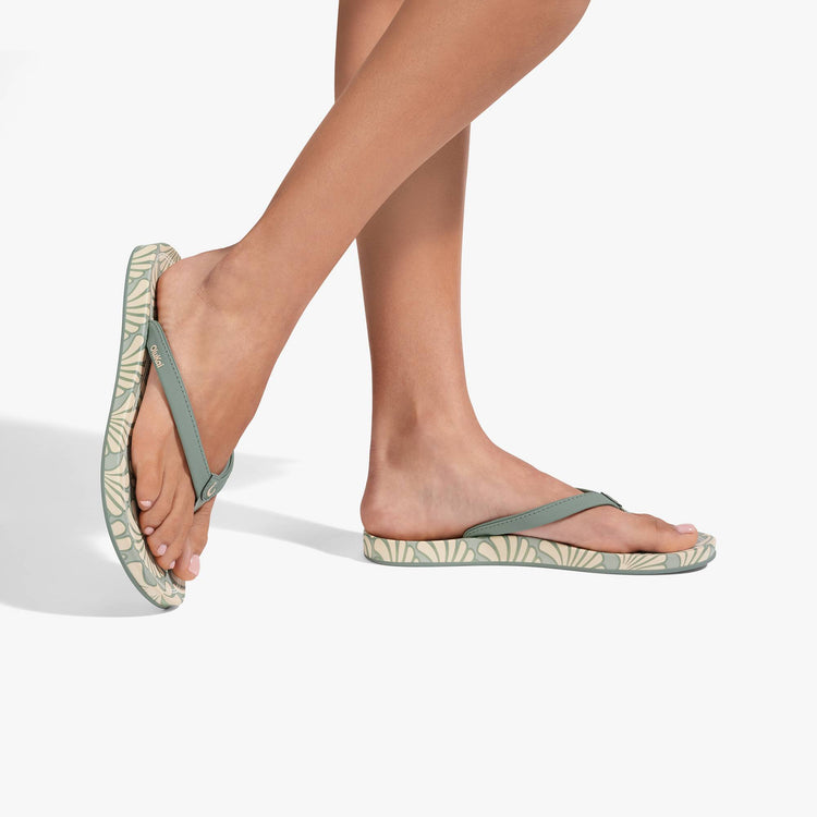 Uiki W flip-flops on feet, green leaf-pattern straps and thong front