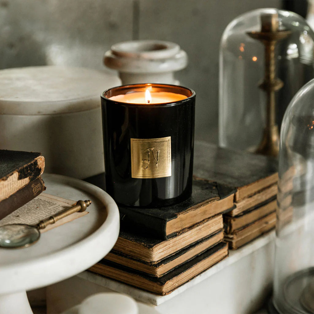 Hudson Candle lit in black glass with gold emblem, vintage books, and antique magnifying glass nearby