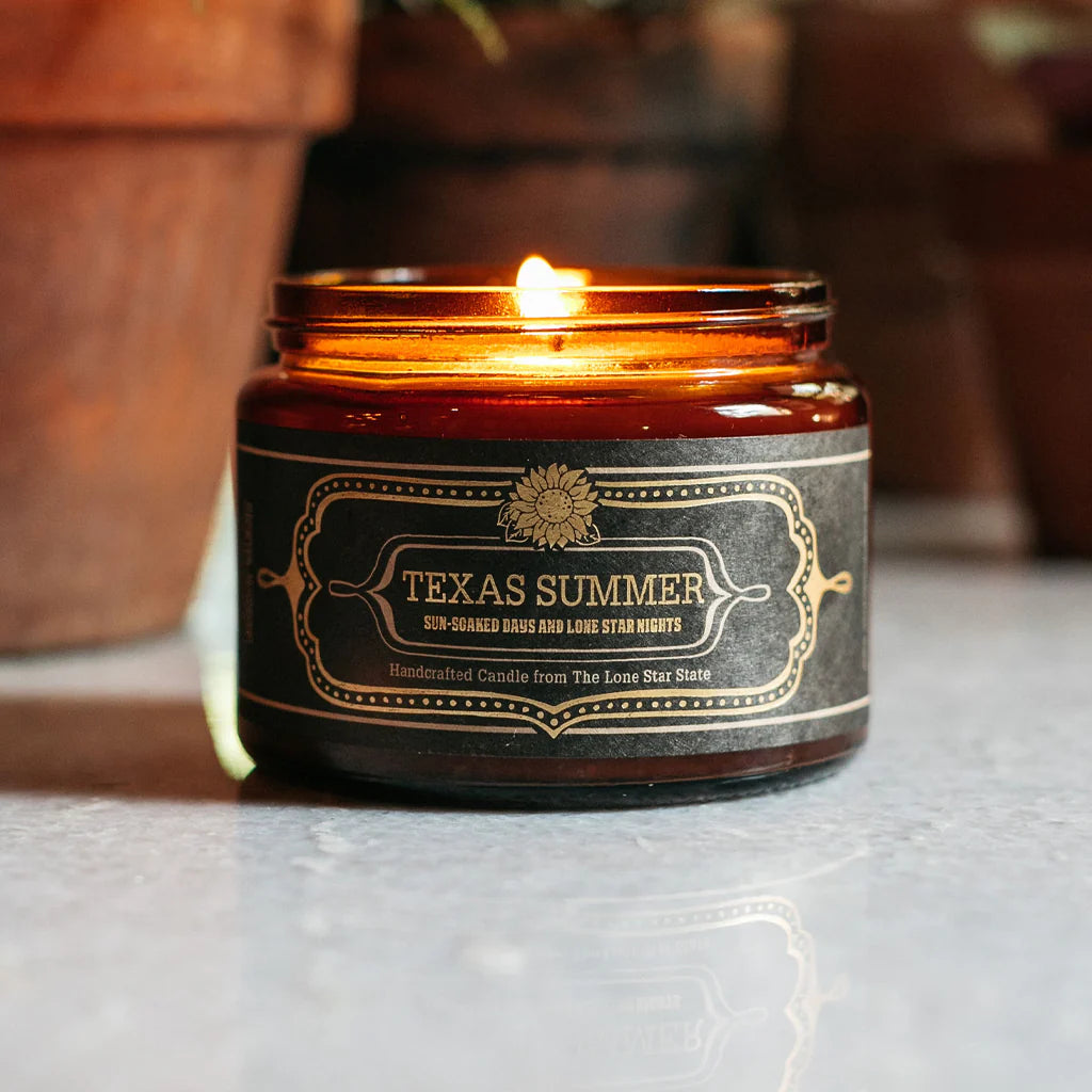 Burning Texas Summer Candle in amber glass jar with vintage-style label, styled in warm, natural setting reflecting authentic Hill Country charm and boutique quality.