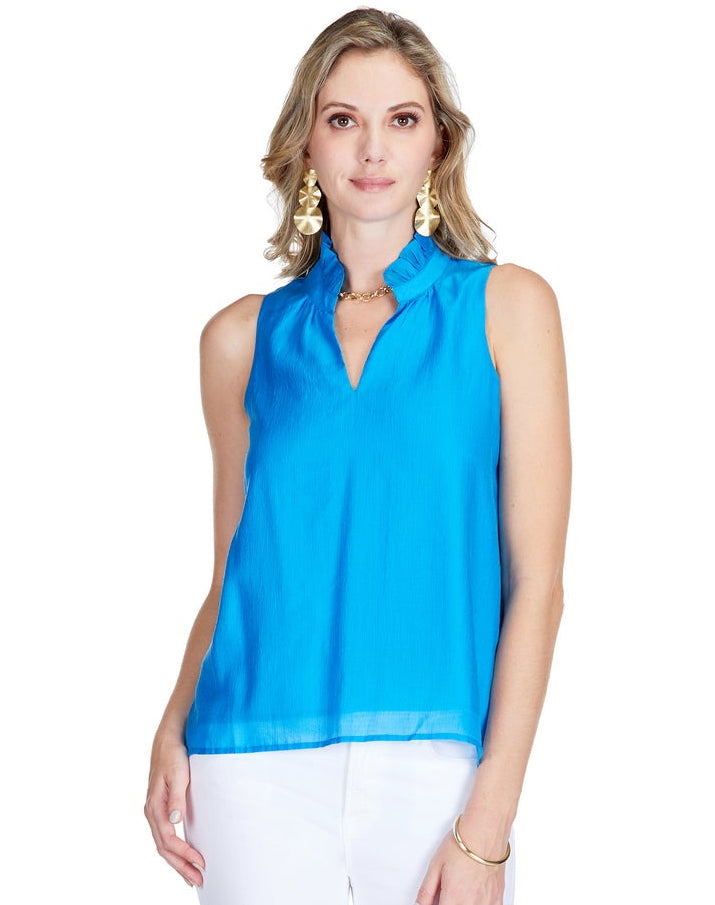 Woman wearing a bright blue sleeveless Ruffles Neck Shell top paired with white cropped pants and clear heeled sandals, styled with gold earrings and bracelet, walking confidently.