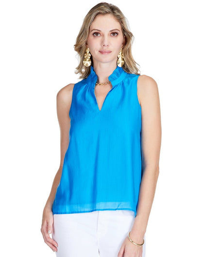 Woman wearing a bright blue sleeveless Ruffles Neck Shell top paired with white cropped pants and clear heeled sandals, styled with gold earrings and bracelet, walking confidently.