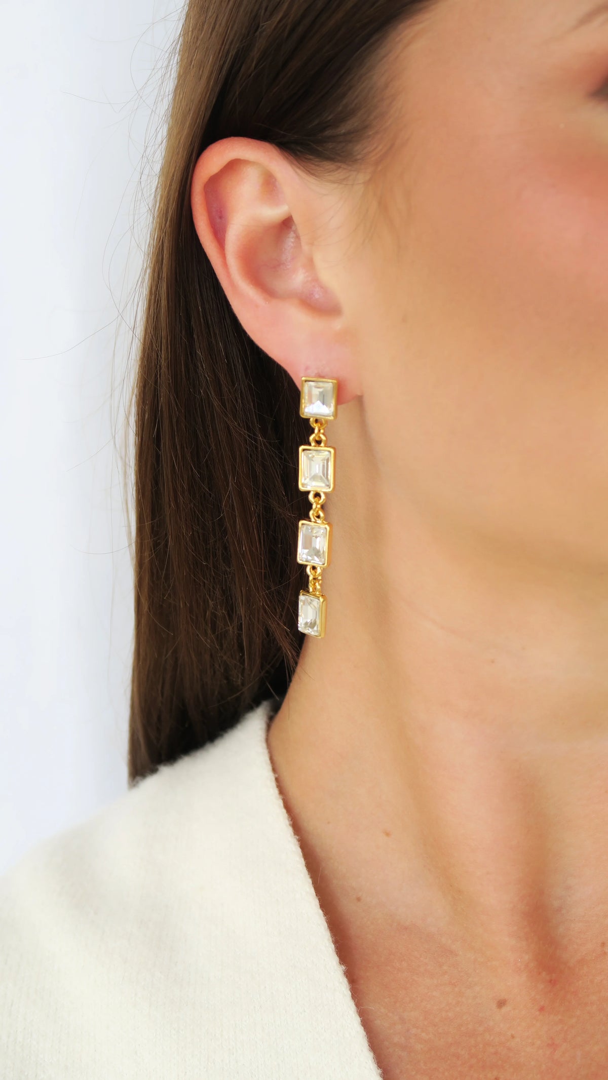 Woman wearing long gold drop earrings with square clear stones