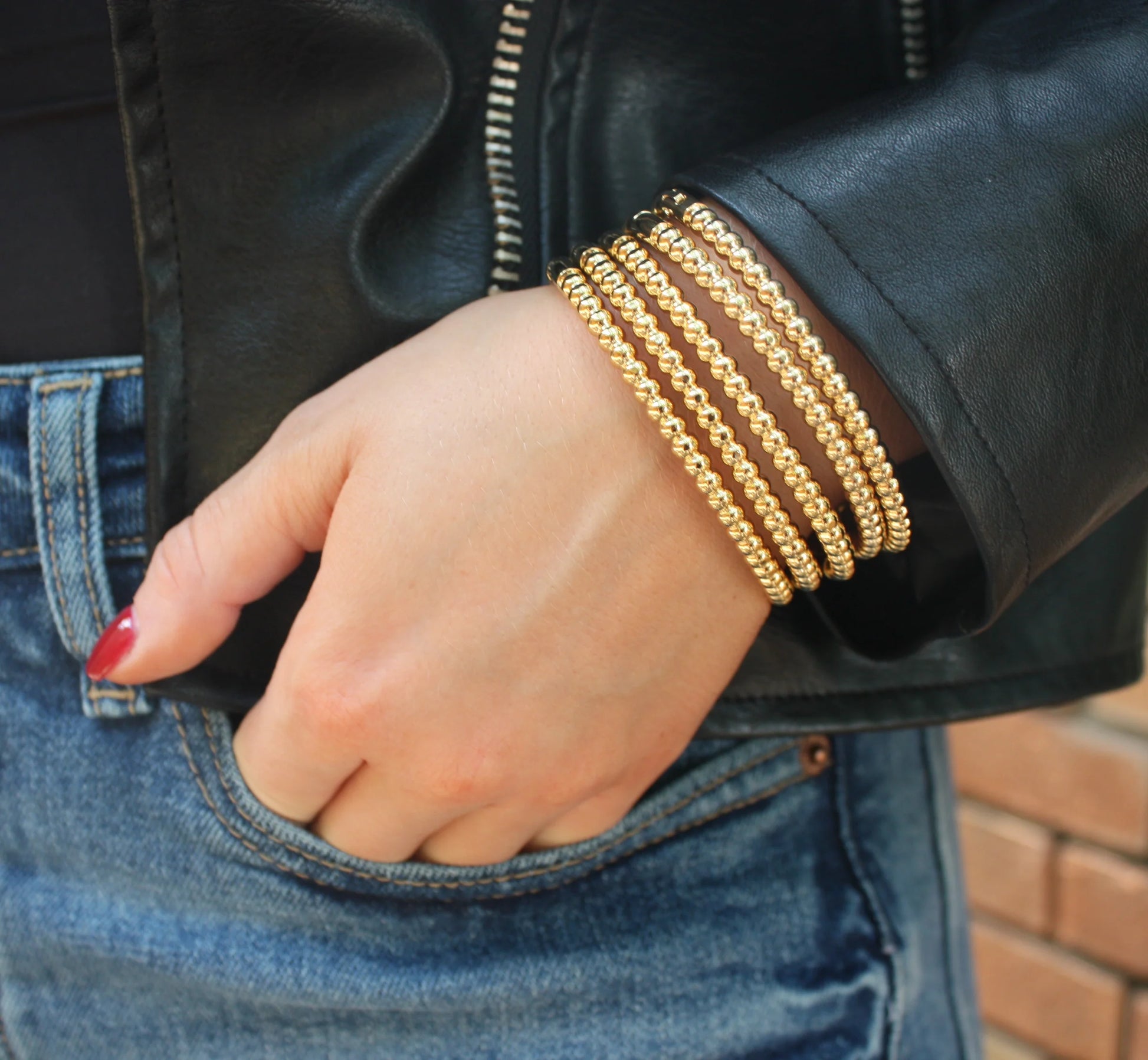 Gold circular repeat bangles stacked on wrist with round bead links