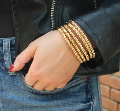 Gold circular repeat bangles stacked on wrist with round bead links