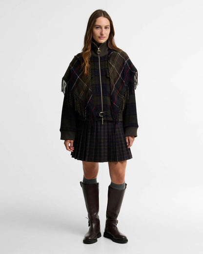 Woman wearing a tartan poncho, pleated skirt, and tall dark boots