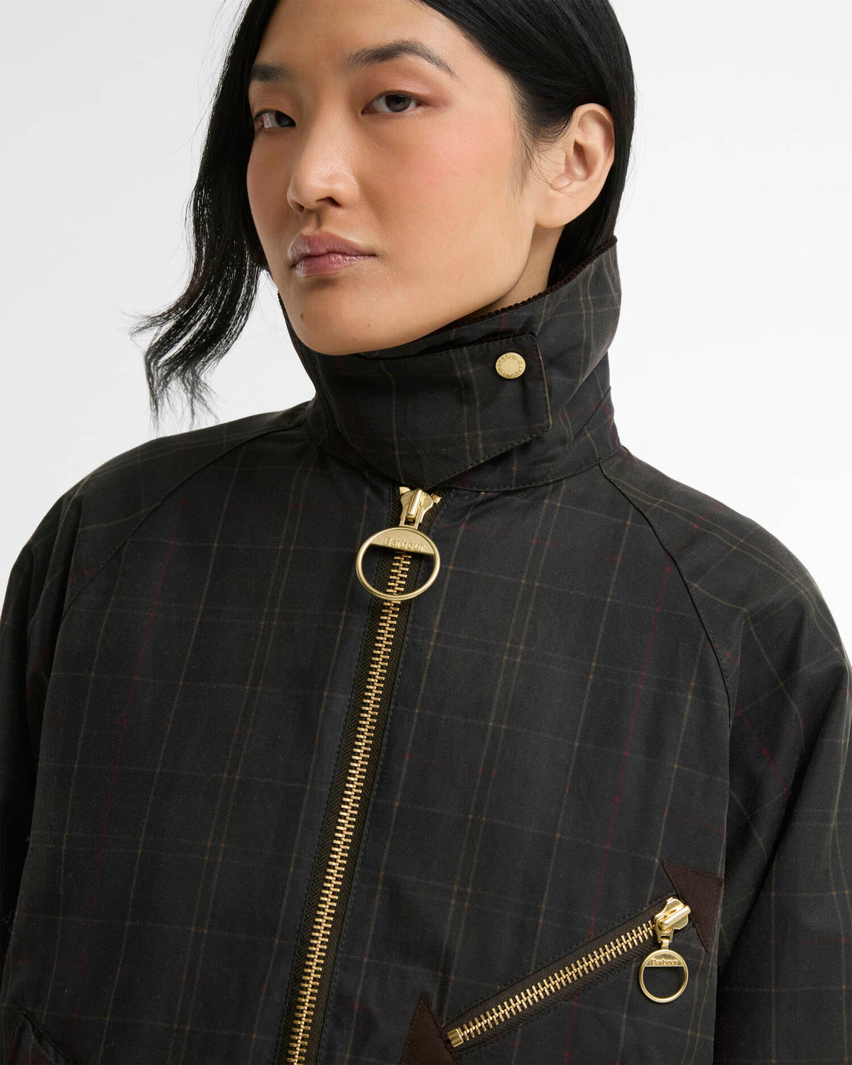 Woman wearing a black plaid high-collar jacket with gold zippers