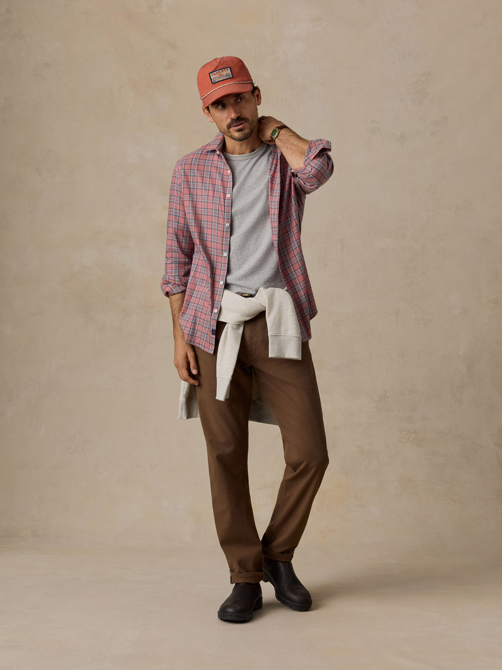 Man in a red plaid shirt, gray T-shirt, brown pants, cap, and black boots