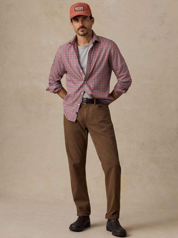Man wearing a red plaid shirt, brown trousers, cap, and black boots