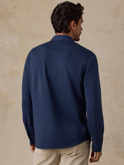 Man seen from behind wearing a navy shirt and beige pants against a neutral wall
