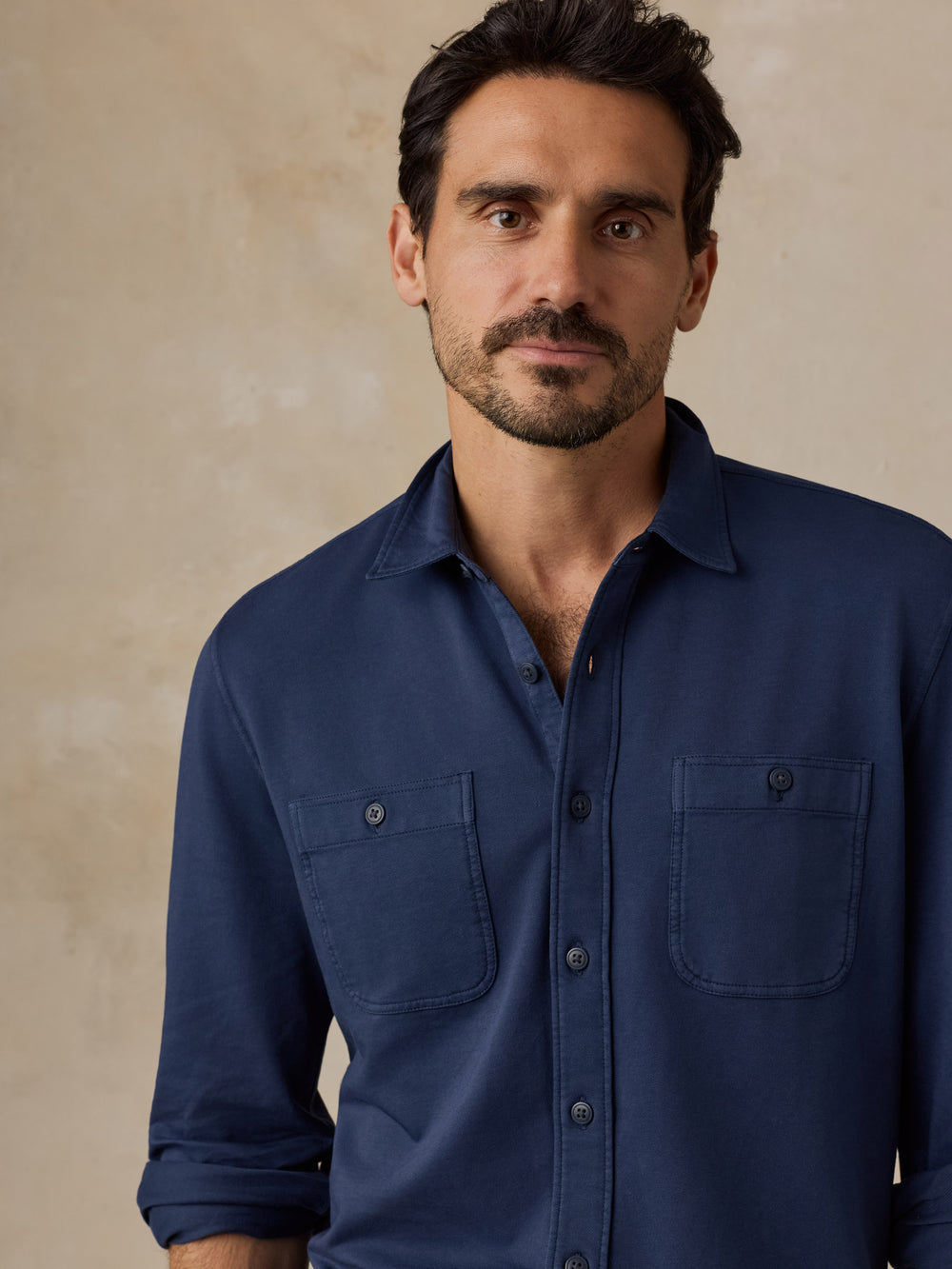 Man wearing a navy blue button-up shirt with two chest pockets against a neutral background