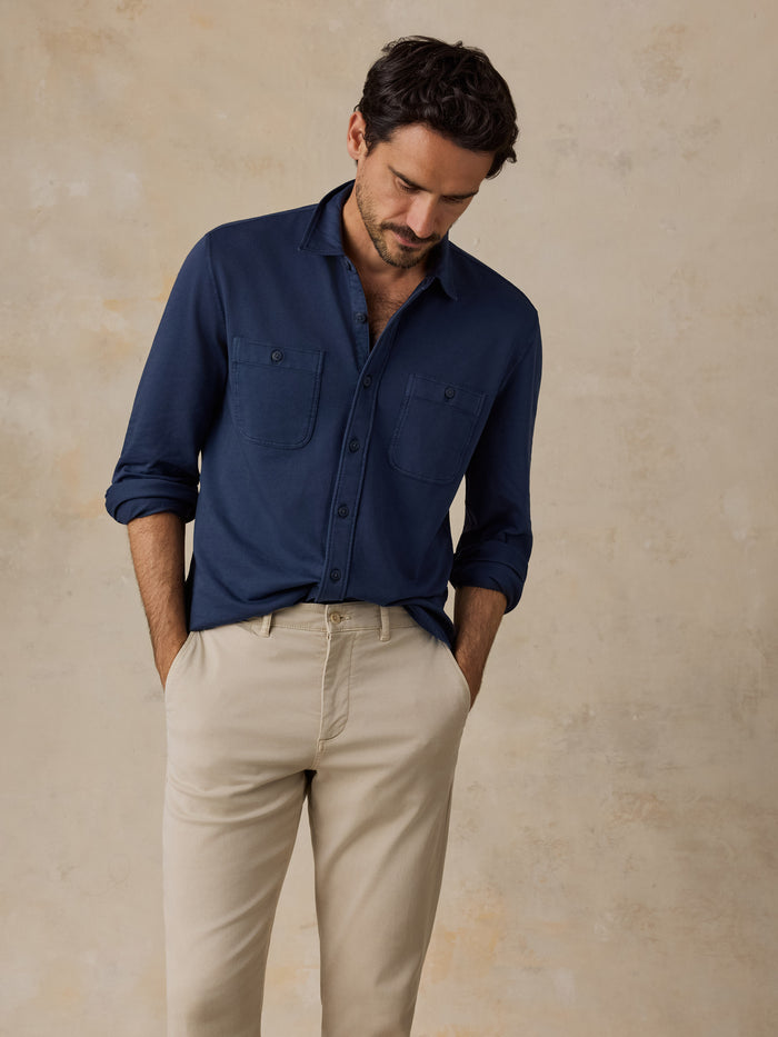 Man wearing a navy button-up shirt and beige pants against a neutral background