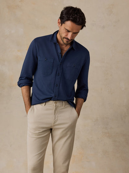 Man wearing a navy button-up shirt and beige pants against a neutral background