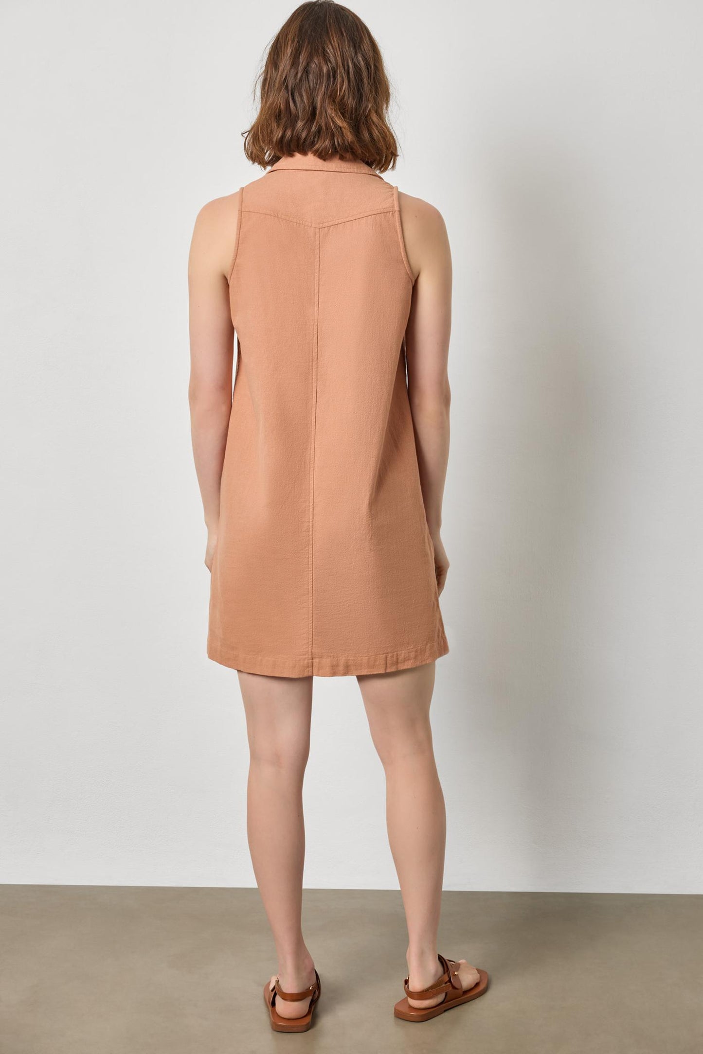 Back view of Sleeveless Pleat Pocket Dress in beige cotton, styled with casual brown sandals