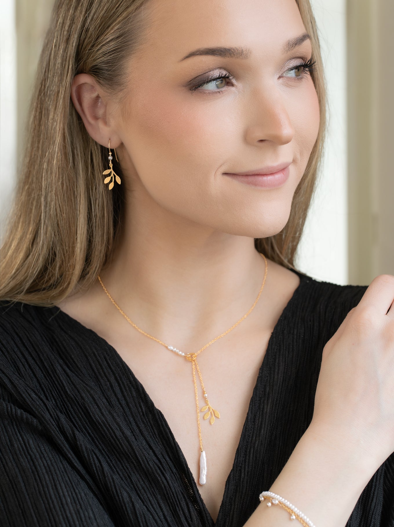 Woman wearing Holly Yashi Signature Earrings, featuring a delicate gold leaf design, paired with a matching gold necklace and pearl bracelet, styled with effortless Hill Country charm.