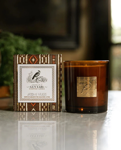 Guy Earl Candle in a brown glass jar beside a patterned decorative box, showcasing artisan home fragrance with a sophisticated, timeless style.