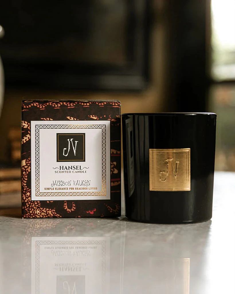 Hansel Candle in a sleek black glass container with a gold emblem, displayed next to its elegant, patterned gift box, reflecting premium boutique home fragrance style.