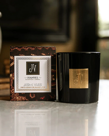 Hansel Candle in a sleek black glass container with a gold emblem, displayed next to its elegant, patterned gift box, reflecting premium boutique home fragrance style.