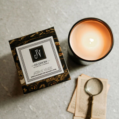 Hudson Candle in dark glass with lit wick, artisan box, and vintage magnifying glass nearby