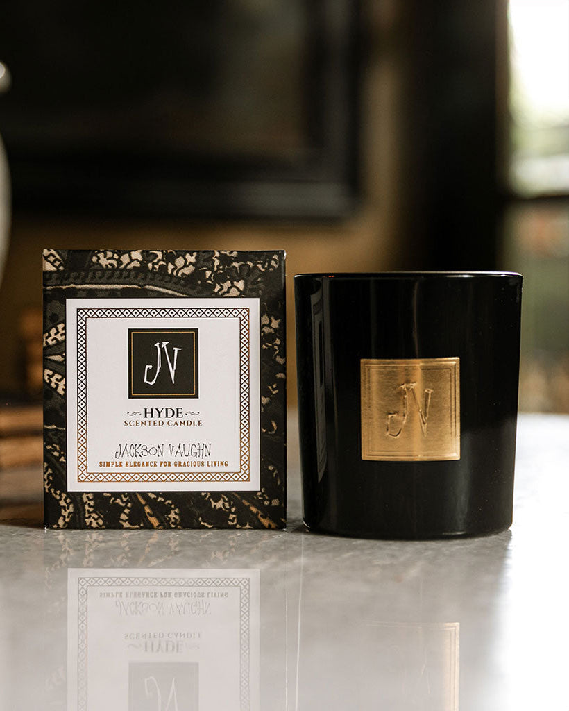 Hyde Candle in a sleek black container with a gold emblem, displayed next to its elegant black and white branded box, reflecting a sophisticated and high-quality home fragrance.