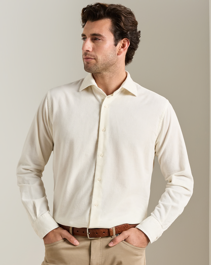 A man wearing a light cream-colored long-sleeve button-down shirt, khaki pants, and a brown leather belt, standing against a neutral beige background.