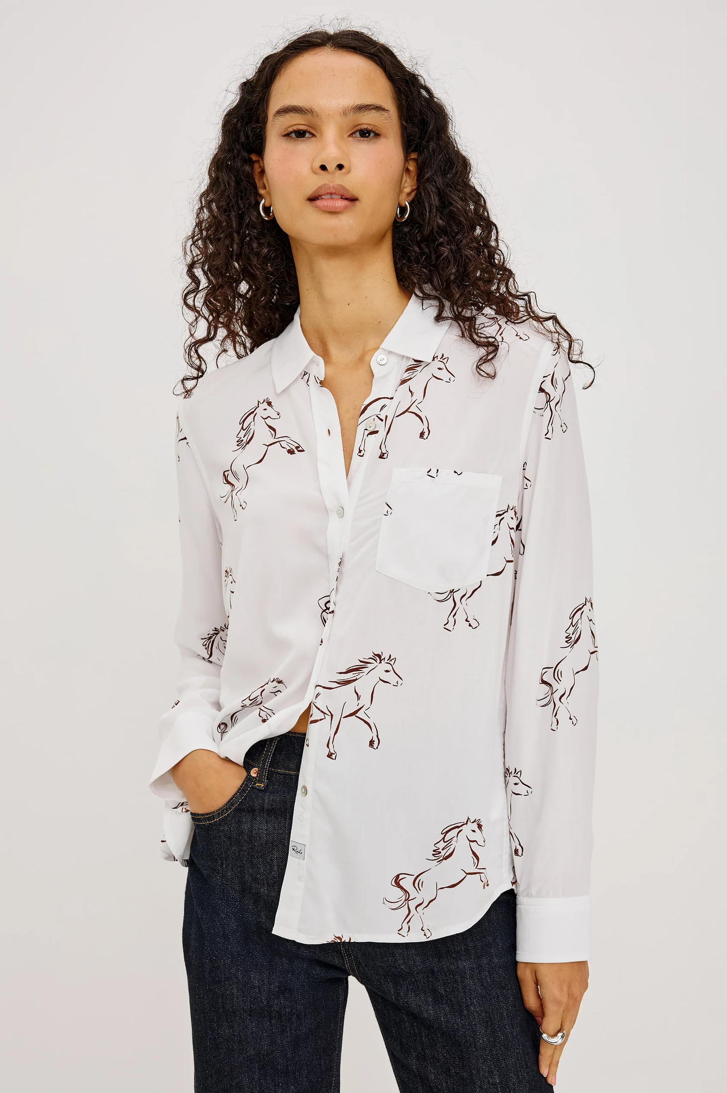 Woman wearing a white illustrated button up shirt and dark jeans
