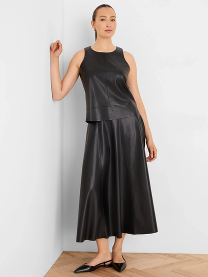 Woman wearing a sleeveless black leather midi dress and pointed flats beside a white wall