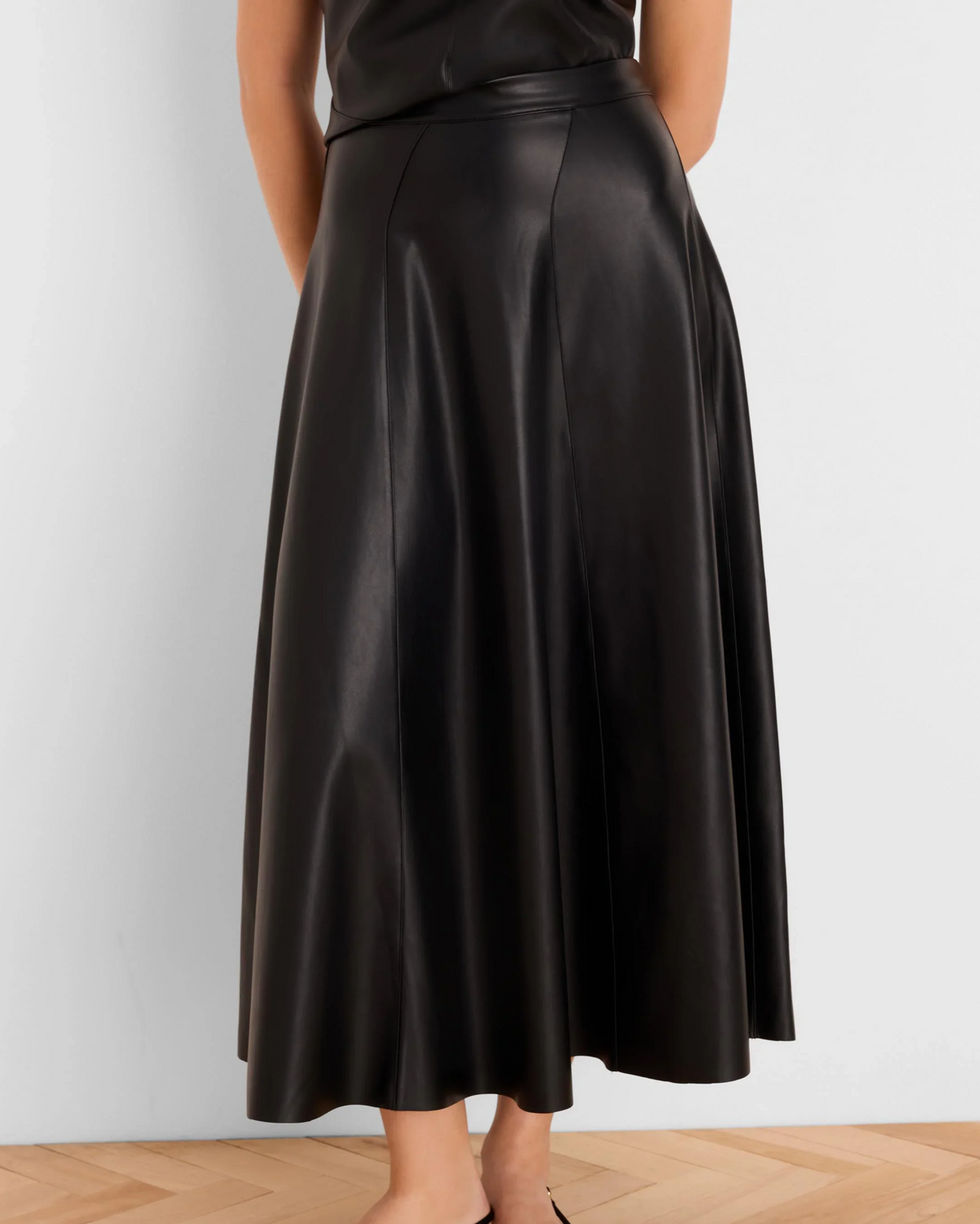 Woman wearing a flowing black leather midi skirt on a wood floor