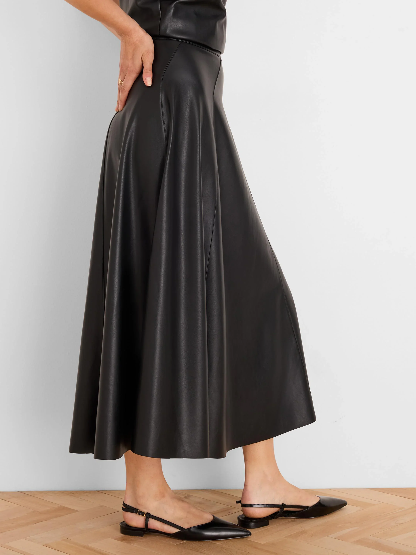 Woman wearing a black leather-look midi skirt and black slingback flats