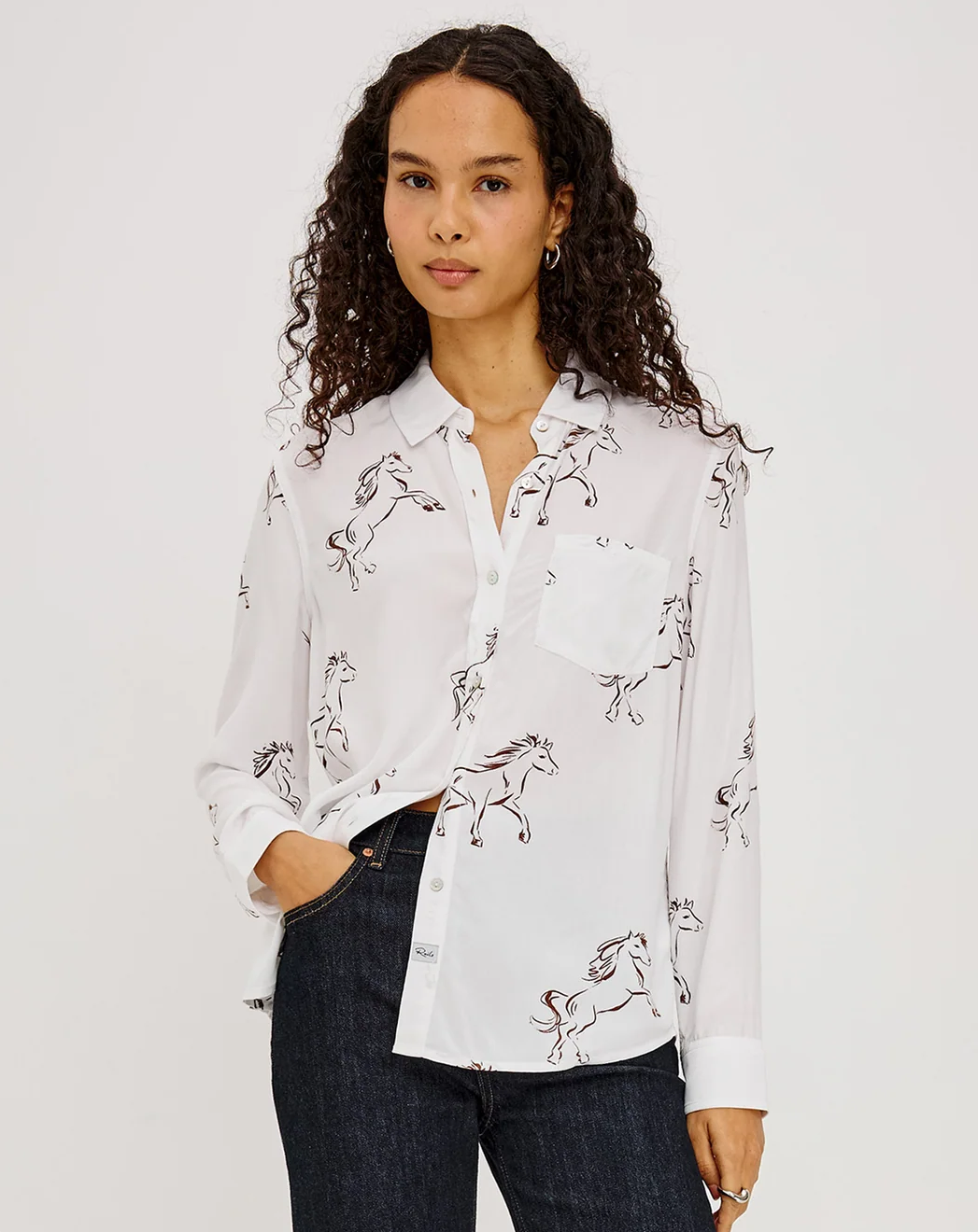 Woman wearing a white horse-print button-up shirt with dark jeans