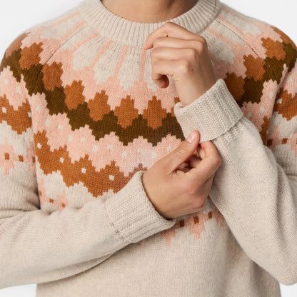 Person wearing a cream sweater with pink and brown geometric patterns adjusting the cuff
