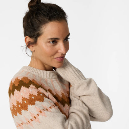 Woman wearing a cream and rust patterned sweater against a light background