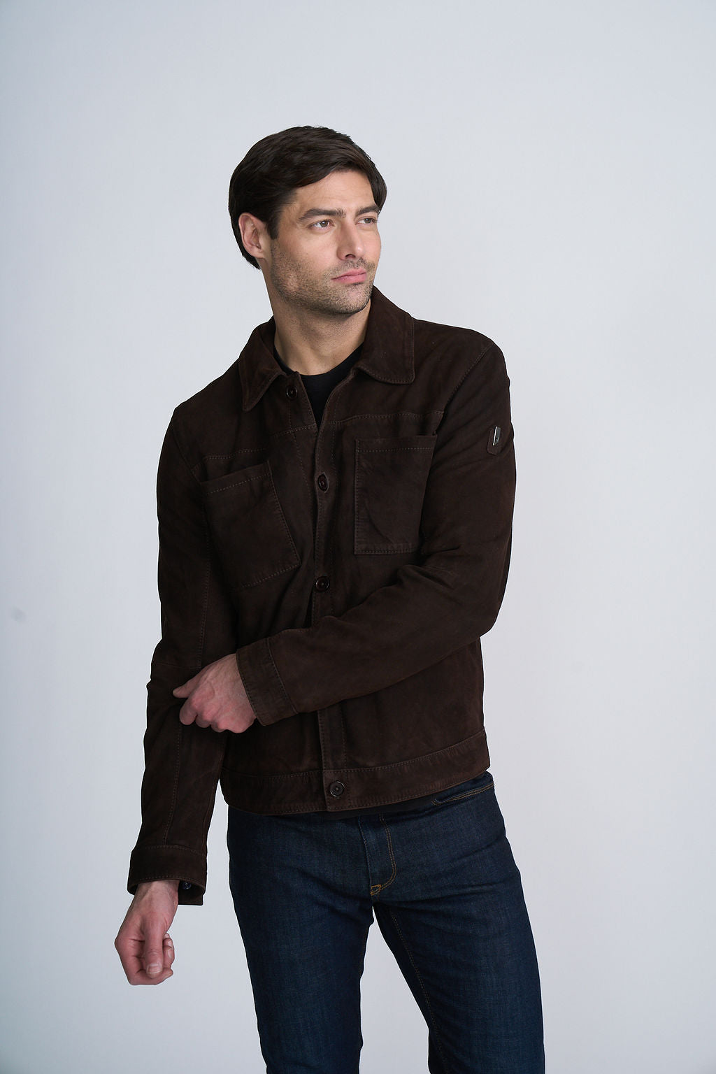 Man wearing a dark brown jacket and jeans against a light background